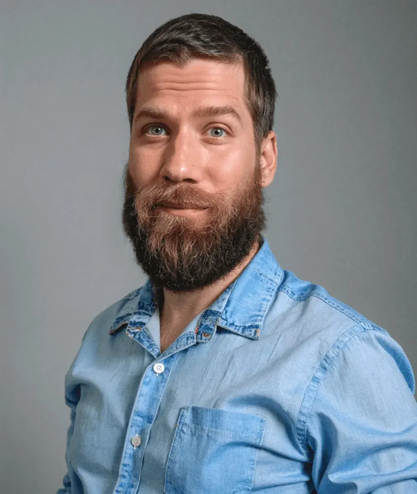 Portrait of James Roberts, a man with short dark hair and a full beard, wearing a light blue denim shirt.